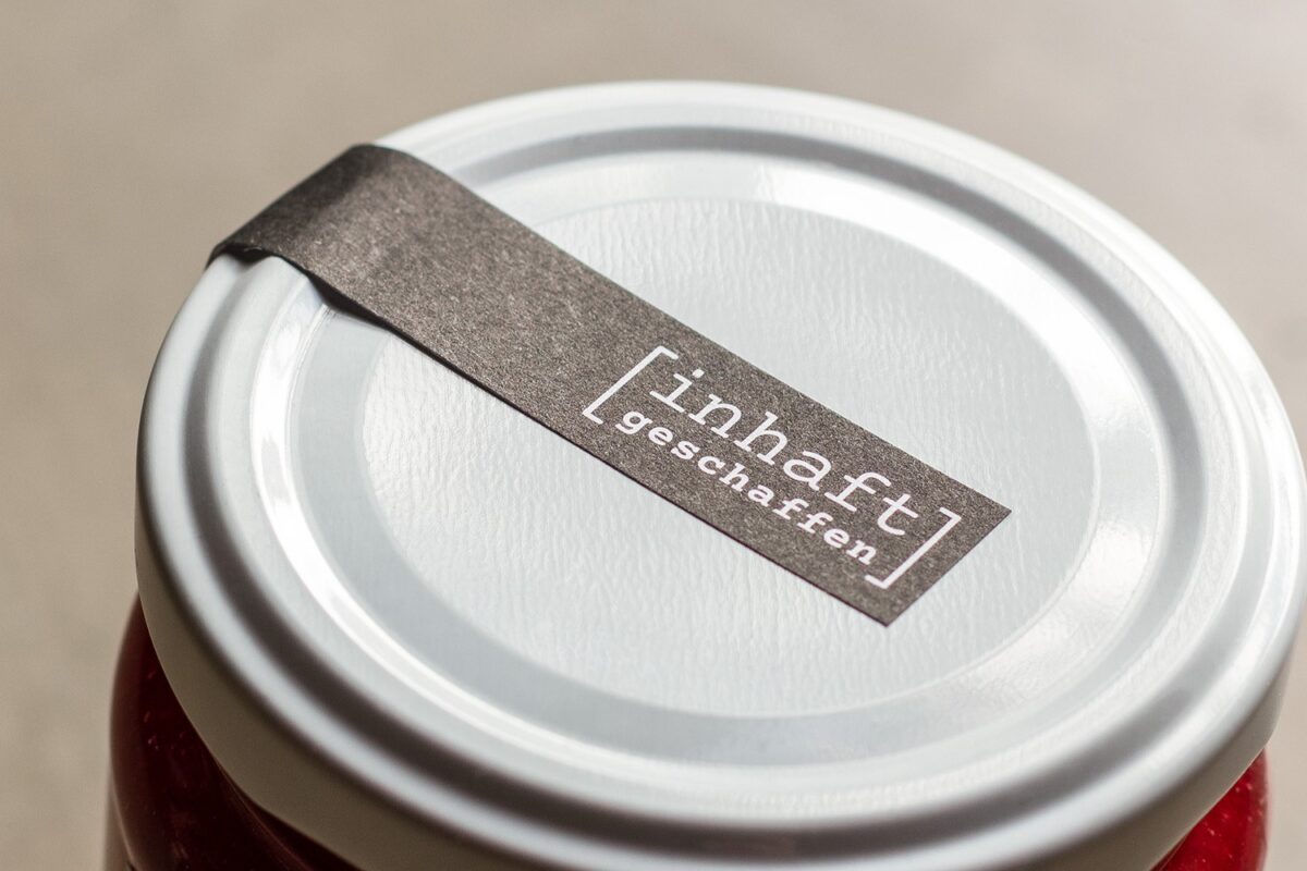 Verschlussband mit Logo «inhaft geschaffen» auf dem Deckel eines Konfitürenglases