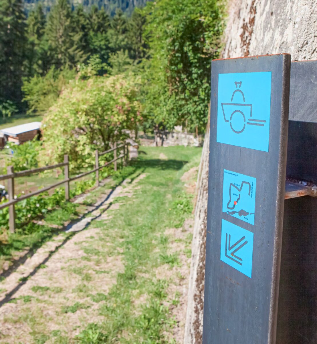 Wegstele des Nollawegs in Thusis mit hellblauen Piktogrammen und Richtungspfeilen