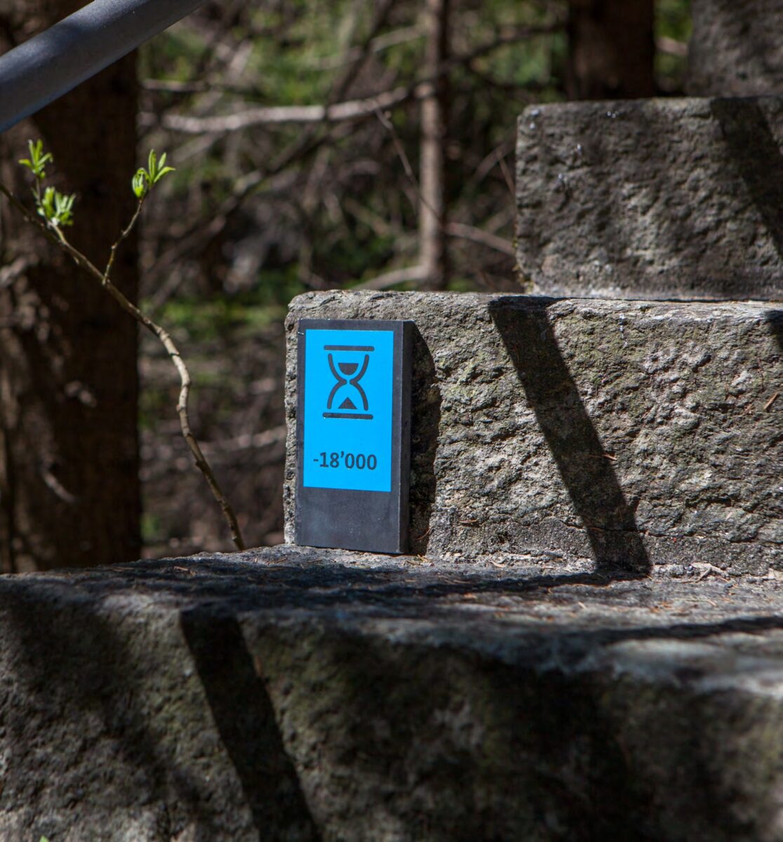 Dunkle Stele mit hellblauem Sanduhr-Piktogramm in der Viamala-Schlucht